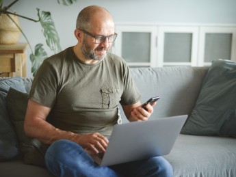 A middle aged man looks at his laptop and phone. 
